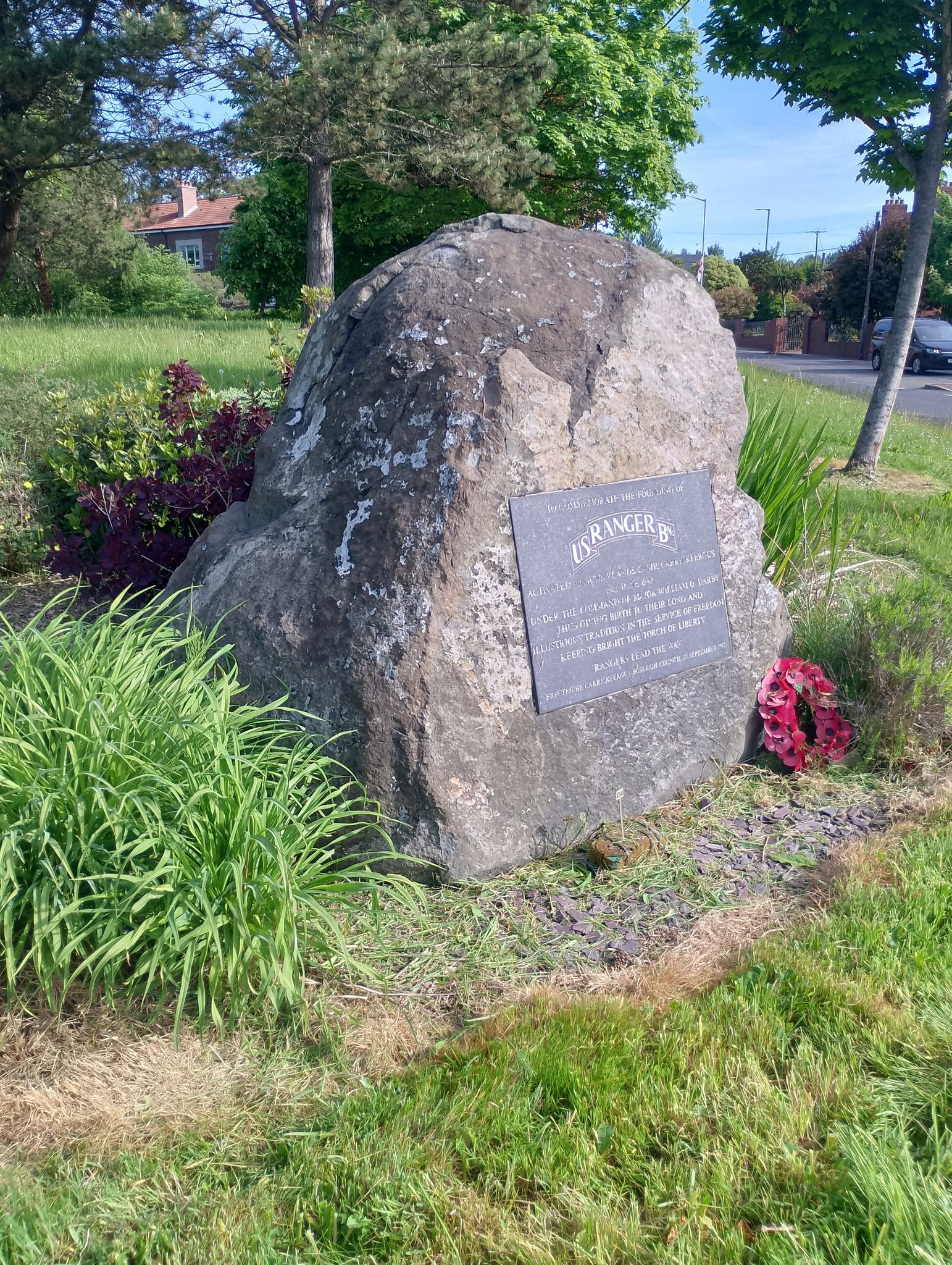 U.S. Ranger memorial stone with plaque and wreath in Carrickfergus, surrounded by grass and trees.